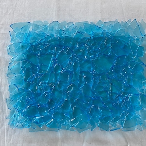 May include: A close-up of a blue mosaic made of many small, irregular pieces of glass. The mosaic is arranged in a rectangular shape and has a slightly textured surface.