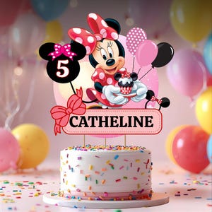 May include: A birthday cake featuring Minnie Mouse. The cake is decorated with a Minnie Mouse figure, balloons, and a sign reading "CATHELINE". The cake is white with colourful sprinkles and a pink ribbon around the base.