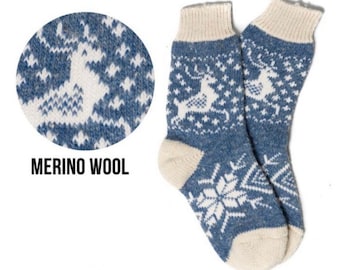 May include: A pair of blue and white knit socks featuring a repeating pattern of reindeer and snowflakes. The socks have a ribbed cuff, a reinforced heel, and a toe section in a solid cream color. The text MERINO WOOL is printed below a circular detail.