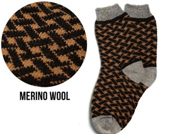 May include: A pair of socks featuring a black and brown geometric pattern with grey cuffs, heels, and toes. The text MERINO WOOL is printed below a circular inset showing a magnified view of the knit texture and the woven pattern details.