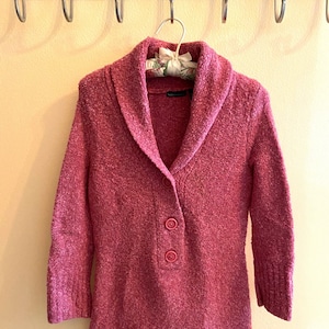 May include: A pink knitted cardigan with a wide collar and three buttons down the front.