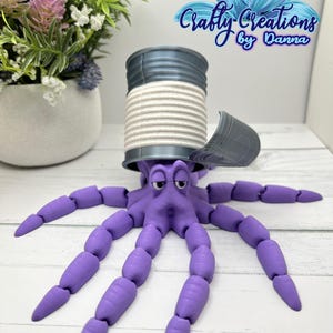 May include: A purple articulated octopus toy emerging from a gray can with a white interior. The octopus has multiple segmented tentacles. The can has a partially open lid. The image includes the text "Crafty Creations by Danna".