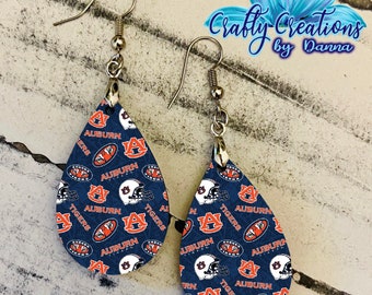 May include: A pair of teardrop-shaped earrings with a blue and orange pattern featuring the Auburn Tigers logo, helmets, and the words "Auburn Tigers".