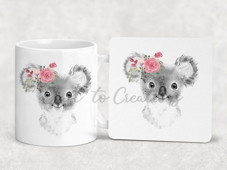 May include: A white ceramic mug featuring a grey koala wearing a pink flower crown. The koala is looking to the right. The mug is accompanied by a matching coaster.
