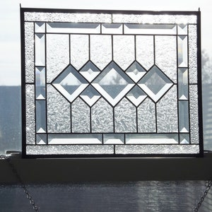 May include: A clear glass stained glass window with a geometric diamond pattern. The window is framed in black metal and has a textured glass surface.