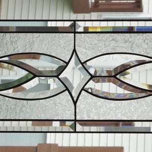 May include: Rectangular stained glass window with a black border. The design features a central diamond shape and curved, leaf-like elements in shades of green, brown, and clear glass. The background is a textured, frosted glass.