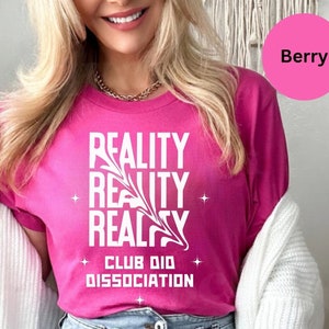 Może przedstawiać: Różowy T-shirt z napisem "REALITY REALITY REALITY CLUB DID DISSOCIATION" w kolorze białym.