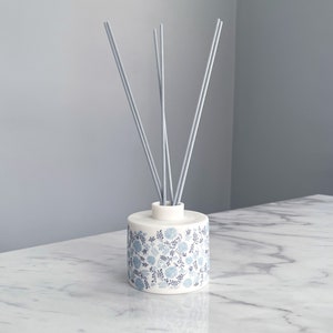 May include: A white ceramic diffuser bottle with a blue and white floral pattern and grey diffuser sticks.