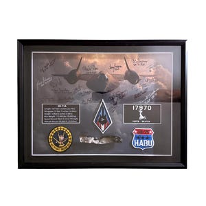 May include: A framed display featuring an SR-71A aircraft image with multiple signatures, a technical data plaque with imperial measurements, a diamond-shaped patch, a metal fragment, a circular 1st Strat Recon Sq patch, and a shield-shaped Habu patch.