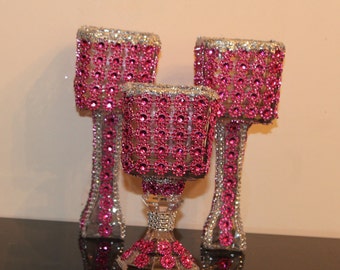 Puede incluir: Tres candelabros decorativos con base plateada y pedrería rosa. Los candelabros tienen forma de copa y cuadrado.