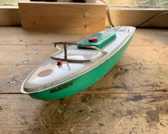 May include: Vintage toy boat with a white and green hull. The boat has a metal frame and a red accent on the front. The word "HAWK" is printed on the side of the boat.