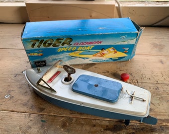 May include: Vintage tin toy boat with a blue and white color scheme, featuring the text "TIGER CLOCKWORK SPEED BOAT" on the box. The boat has a wind-up key and a red button. A classic collectible toy.