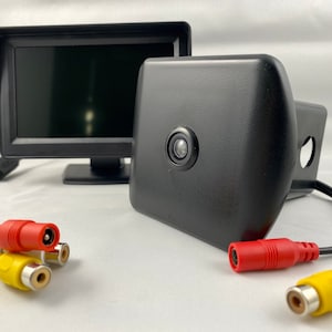 May include: A black rear view camera with a black monitor and yellow and red RCA cables. The camera is mounted on a black bracket.