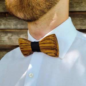 Puede incluir: Una pajarita de madera con una banda negra. La pajarita est&aacute; hecha de madera marr&oacute;n oscura con un patr&oacute;n de veta natural.