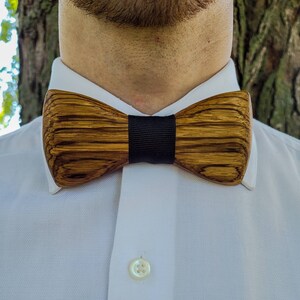 Puede incluir: Una pajarita de madera con una banda negra. La pajarita tiene un patr&oacute;n de veta de madera marr&oacute;n y marr&oacute;n oscuro.