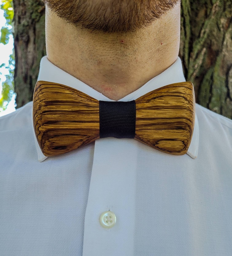 Puede incluir: Una pajarita de madera con una banda negra. La pajarita tiene un patr&oacute;n de veta de madera marr&oacute;n y marr&oacute;n oscuro.