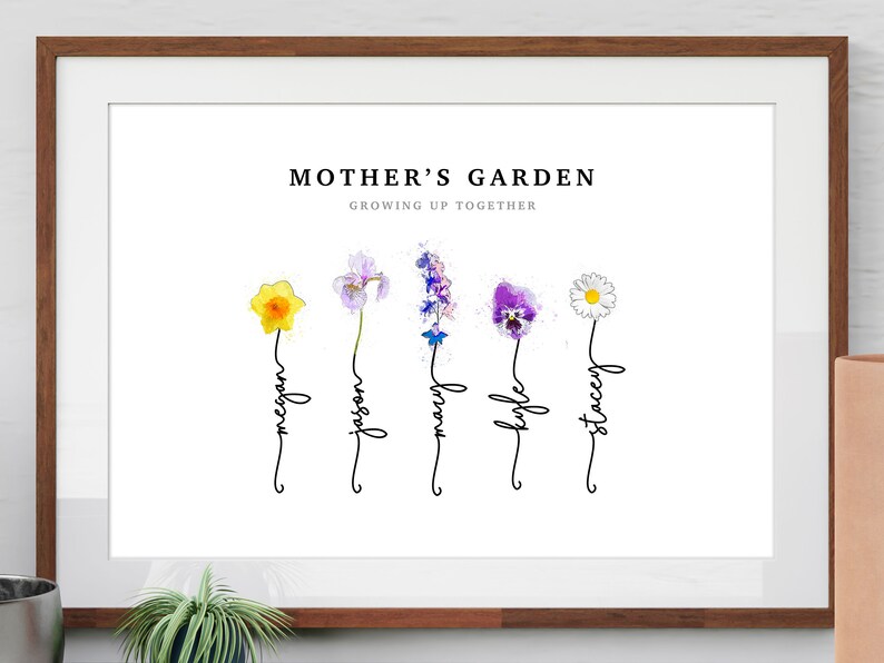 Mother's Garden personalized birth flower print in a wood frame with white mat, leaning on a shelf beside a plant. Five watercolor birth month flowers (daffodil, iris, larkspur, violet and daisy) grow from hand-lettered stems that spell each name. Custom family birth flower art, also made as Grandma's Garden for a sentimental grandma gift.