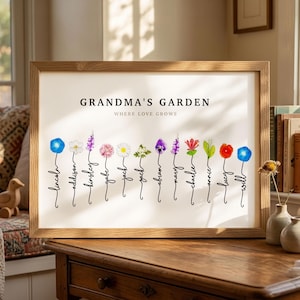 Grandma's Garden personalized birth flower print in a light wood frame, resting on a dresser in a sunlit room. Subtitle reads Where Love Grows. Twelve watercolor birth month flowers, including morning glory, narcissus, larkspur, daisy, hawthorn, violet, honeysuckle, lily of the valley and poppy, each grow from a hand-lettered stem that spells one grandchild's name. A sentimental grandma gift from all the grandkids.