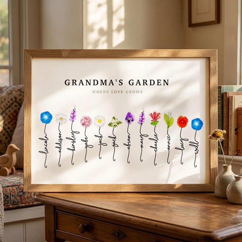 Grandma's Garden personalized birth flower print in a light wood frame, resting on a dresser in a sunlit room. Subtitle reads Where Love Grows. Twelve watercolor birth month flowers, including morning glory, narcissus, larkspur, daisy, hawthorn, violet, honeysuckle, lily of the valley and poppy, each grow from a hand-lettered stem that spells one grandchild's name. A sentimental grandma gift from all the grandkids.