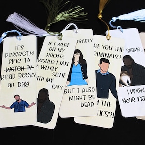 Può includere: Una collezione di segnalibri fatti a mano con nappe decorative. Ogni segnalibro presenta una citazione unica e un'illustrazione di cartoni animati. Le citazioni sono in nero su sfondo crema. Le nappe sono in vari colori.