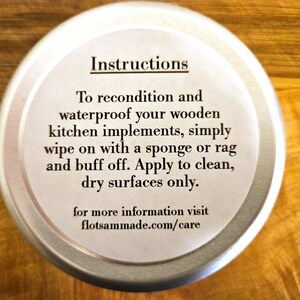 May include: A round silver metal tin with a white label featuring black text that reads: Instructions. To recondition and waterproof your wooden kitchen implements, simply wipe on with a sponge or rag and buff off. Apply to clean, dry surfaces only. for more information visit flotsammade.com/care