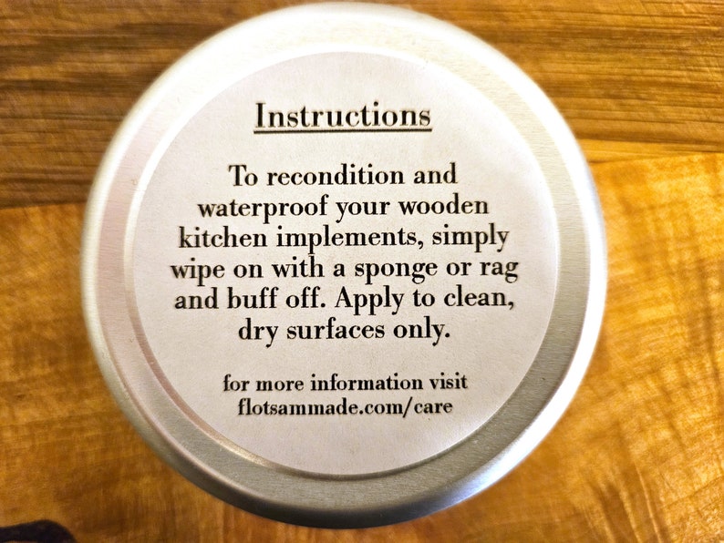 May include: A round silver metal tin with a white label featuring black text that reads: Instructions. To recondition and waterproof your wooden kitchen implements, simply wipe on with a sponge or rag and buff off. Apply to clean, dry surfaces only. for more information visit flotsammade.com/care