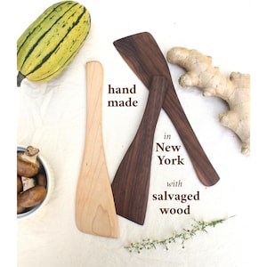 May include: Handmade wooden spatulas in light and dark wood tones. The image includes text that reads "hand made in New York with salvaged wood". A squash, ginger, and mushrooms are also in the image.