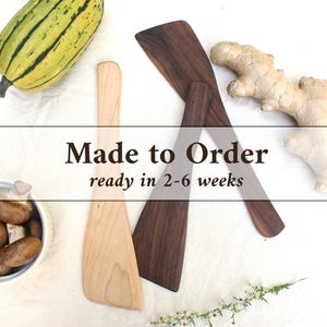 May include: Two wooden spatulas, one light-colored and one dark-colored, positioned near a striped squash, a piece of ginger, a small bowl of mushrooms, and a sprig of flowers. The text "Made to Order ready in 2-6 weeks" is overlaid on the image.