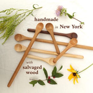 May include: A collection of handmade wooden spoons in various shades of brown, with the text "handmade in New York with salvaged wood." The spoons are arranged on a white surface with floral accents.