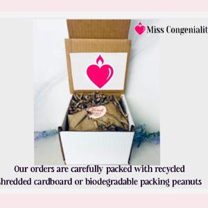 May include: A white box with a brown lid is open, revealing shredded paper inside. The box has a pink heart with a flame on top and the text "Miss Congeniality" on the lid. The text "Our orders are carefully packed with recycled shredded cardboard or biodegradable packing peanuts" is below the box.