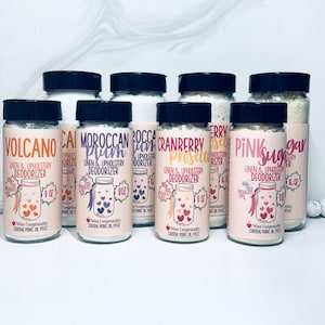 May include: Eight glass jars with white powder inside and black lids. Each jar has a label with a different scent name and a heart design. The scents are Volcano, Calamondin, Moroccan Plum, Rocca, Cranberry Prosecco, Cherry, Pink Sugar, and Lavender.