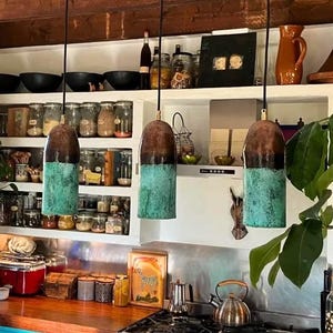 Peut inclure: Trois lampes suspendues avec un dessus en cuivre et un fond turquoise sont suspendues au-dessus d'un comptoir de cuisine. La cuisine comprend un comptoir en bois, des armoires turquoise et une cuisinière en acier inoxydable. Des étagères sont remplies de bocaux et d'ustensiles de cuisine.