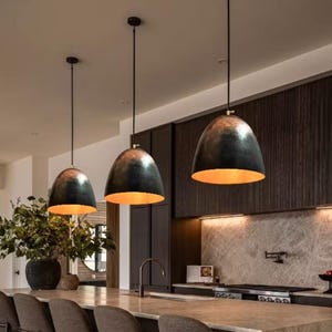 以下が含まれることがあります： ゴールドの内装が施された黒いペンダントライト3つが、バーチェアのあるキッチンアイランドの上に吊り下げられています。ライトはモダンなスタイルで、ハンマードメタル仕上げになっています。