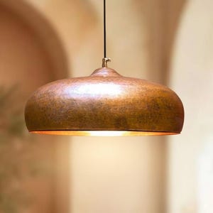 May include: A copper pendant light with a rounded shade. The light hangs from a black cord and has a brass fitting. The interior of the shade glows with a warm light. The light fixture is a stylish addition to any room.