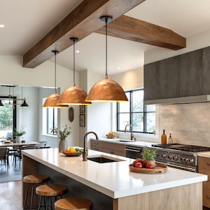 Puede incluir: Tres lámparas colgantes de cobre sobre una isla de cocina con encimera blanca y armarios de madera. La isla tiene un fregadero y una barra de desayuno con taburetes.