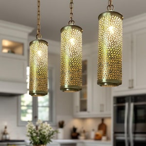 Peut inclure: Trois lampes suspendues dorées avec un design cylindrique perforé pendent de chaînes dans un décor de cuisine.