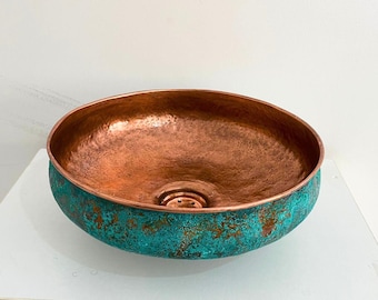 May include: A copper sink with a hammered finish and a turquoise patina. The sink is round and has a drain in the center.