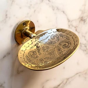 Peut inclure: Un porte-savon en or avec un motif gravé orné. Le porte-savon est fixé au mur avec un support décoratif.