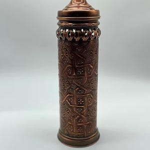 May include: A copper cylindrical container with an intricate geometric pattern and a lid. The container has a decorative openwork design around the top.
