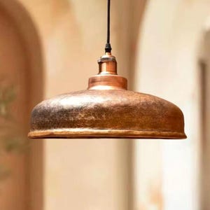 Peut inclure: Un luminaire suspendu en cuivre avec une finition martelée. La lumière a un design simple et un aspect chaleureux et rustique.