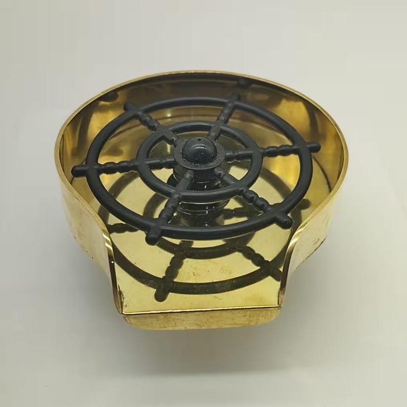 May include: A brass ashtray with a black plastic ship's wheel design in the center.
