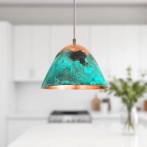 Puede incluir: Una l&aacute;mpara colgante de color turquesa y cobre con un acabado desgastado. La l&aacute;mpara est&aacute; colgada de un techo blanco en una cocina.