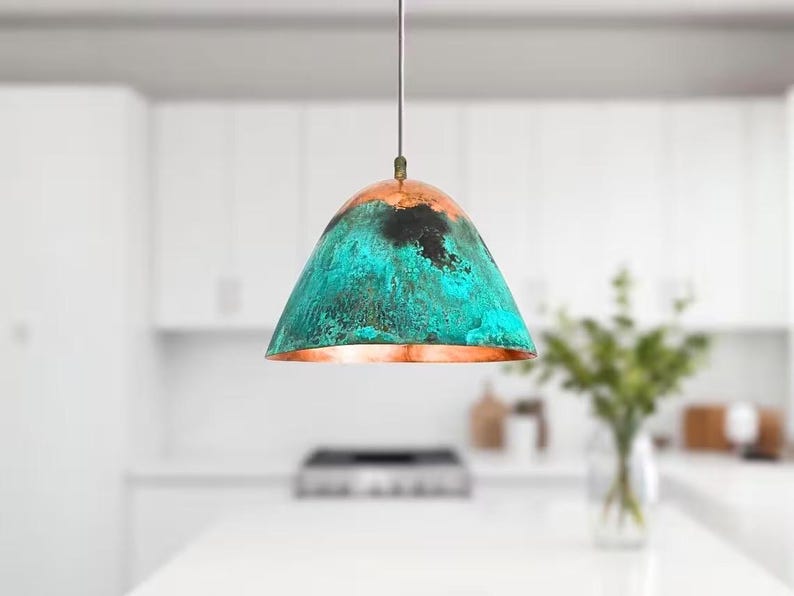 Puede incluir: Una l&aacute;mpara colgante de color turquesa y cobre con un acabado desgastado. La l&aacute;mpara est&aacute; colgada de un techo blanco en una cocina.