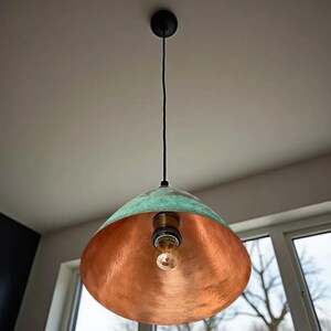 Puede incluir: Una l&aacute;mpara colgante de cobre con un acabado de p&aacute;tina verde. La luz tiene una pantalla redonda en forma de c&uacute;pula y cuelga de un cable negro.