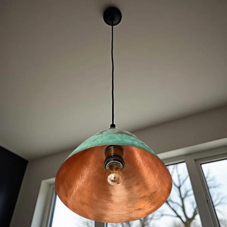 Puede incluir: Una l&aacute;mpara colgante de cobre con un acabado de p&aacute;tina verde. La luz tiene una pantalla redonda en forma de c&uacute;pula y cuelga de un cable negro.