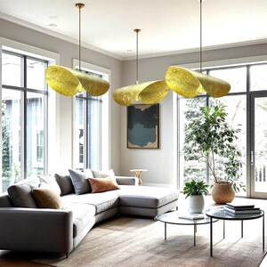 Könnte beinhalten: Drei goldfarbene, gewebte Pendelleuchten hängen von der Decke in einem Wohnzimmer mit einem grauen Ecksofa, zwei Couchtischen und einer großen Topfpflanze.
