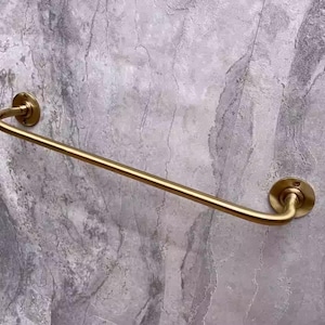 May include: A gold-toned metal towel bar with rounded ends. The bar is mounted to a wall with two round brackets.