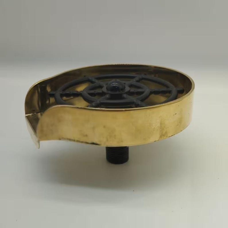 May include: A brass and black metal decorative fountain with a wheel design. The fountain has a curved spout and a threaded base.