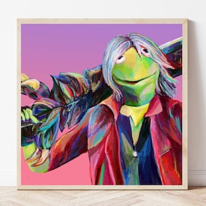 May include: A framed art print featuring a stylized Kermit the Frog character with long, silver hair and a red jacket. The artwork has a vibrant color palette with shades of green, red, purple, and yellow. The background is a gradient of pink and purple.
