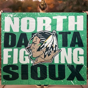May include: Green blanket with the words "NORTH DAKOTA FIGHTING SIOUX" in white and black lettering. The blanket features a Native American head logo in the center. The blanket is held up by a person.